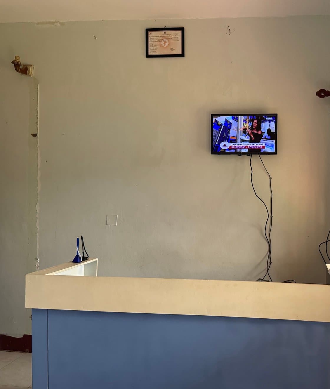 The front desk at Shalom Clinic, with the wall television and the framed licence